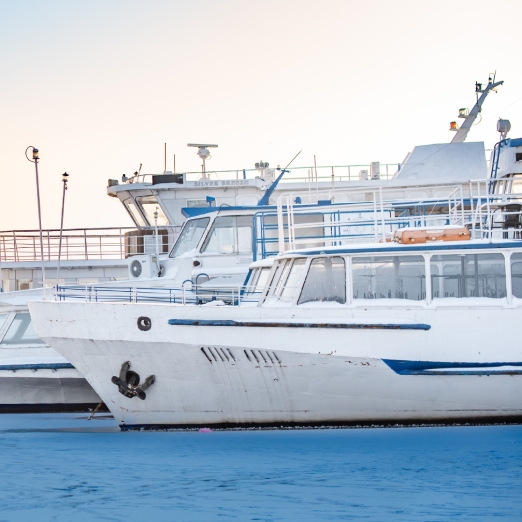 A serene, eye-level shot of several boats, likely ferries or tour boats, docked in a frozen harbor during winter
